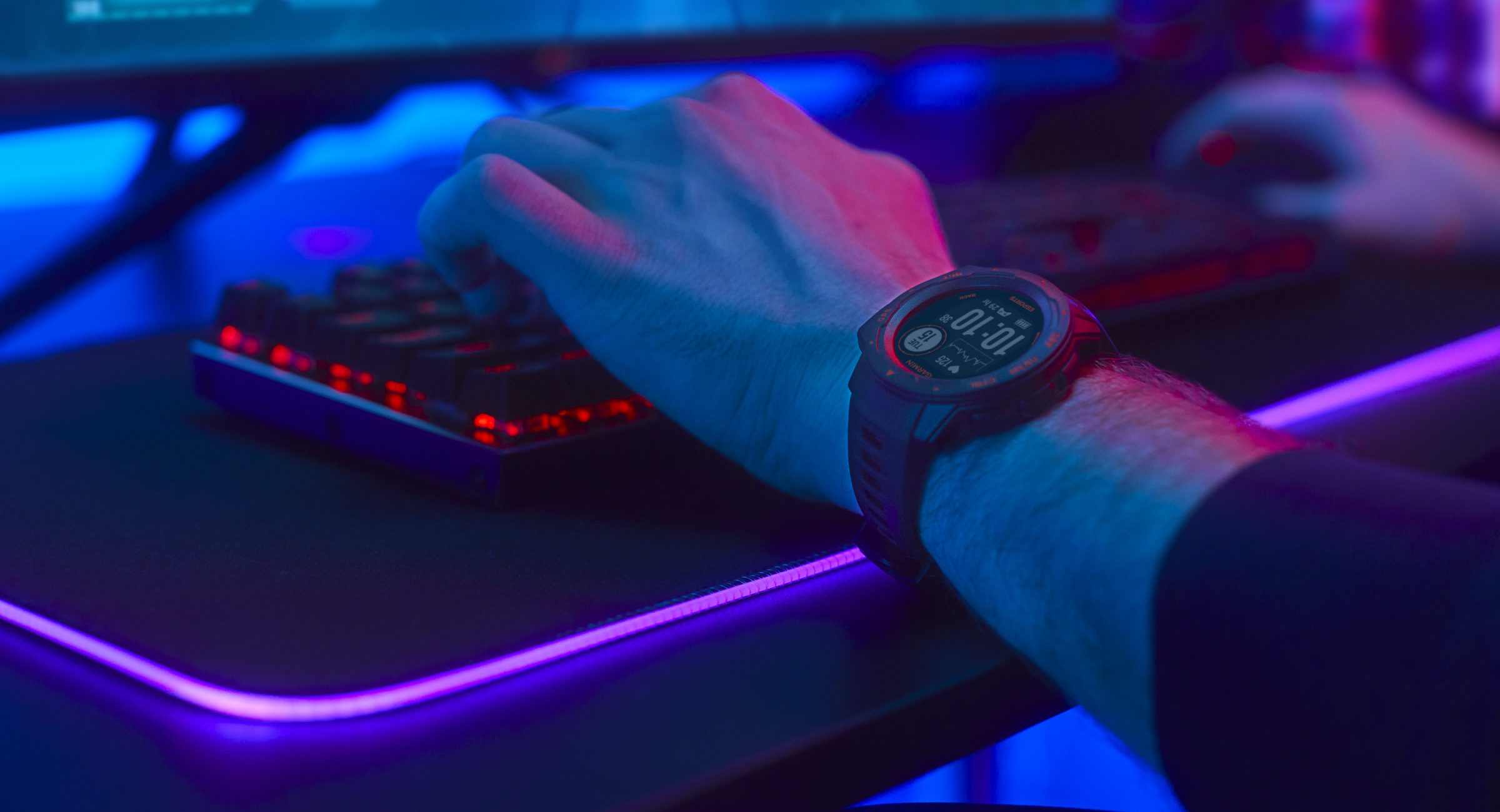 A gamer playing at a computer with a Garmin Instinct Esports Edition smartwatch on