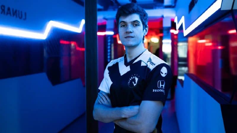 Barney "Alphari" Morris stands with his arms folded wearing a Team Liquid jersey in a dark hallway lit up with varied colored lights.